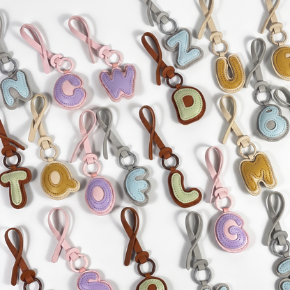 Charm lettre effet cuir avec son anneau metal et sa laniere a nouer, sur fond blanc